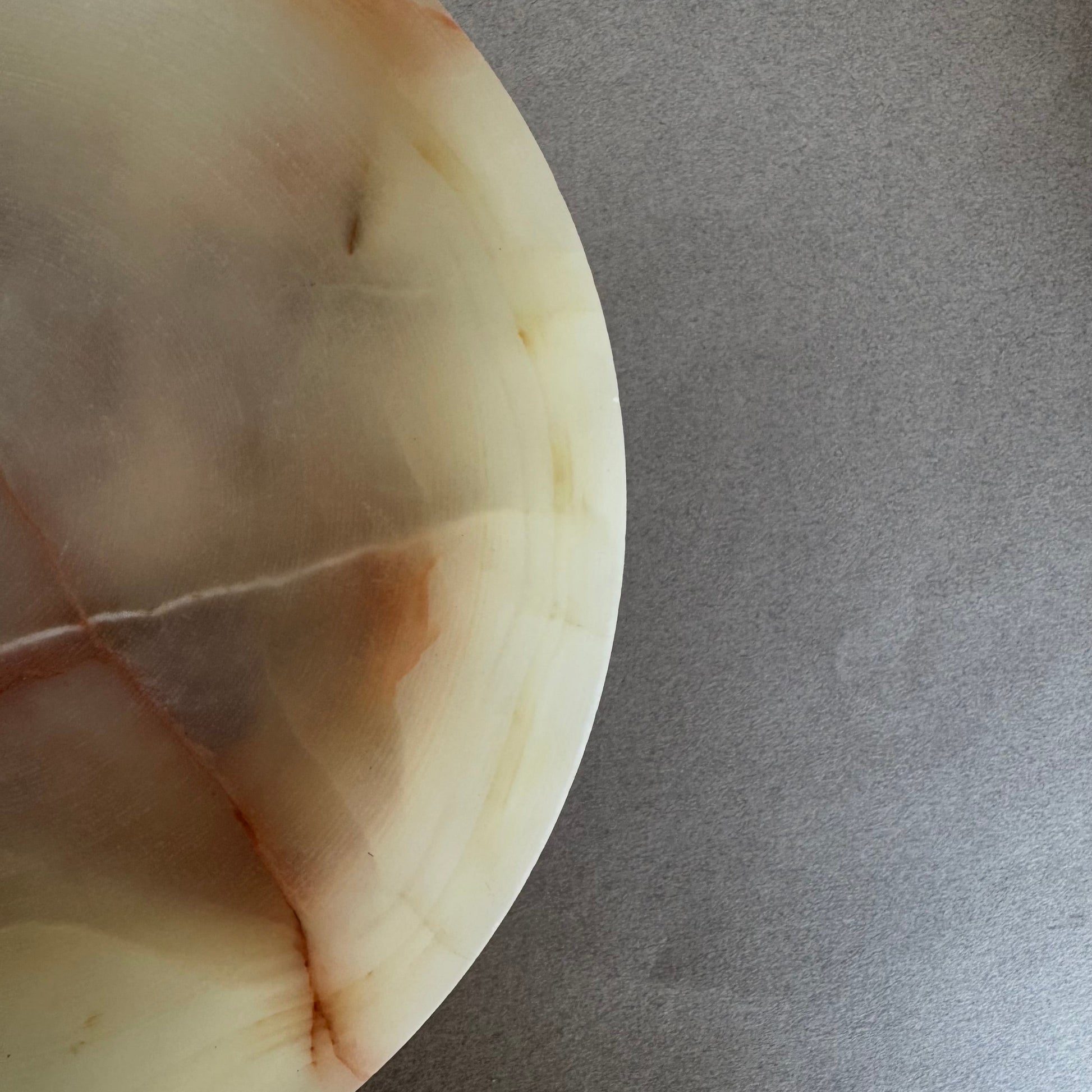 Cream and sage onyx bowl with pedestal base, partially lit to highlight stone’s translucency.