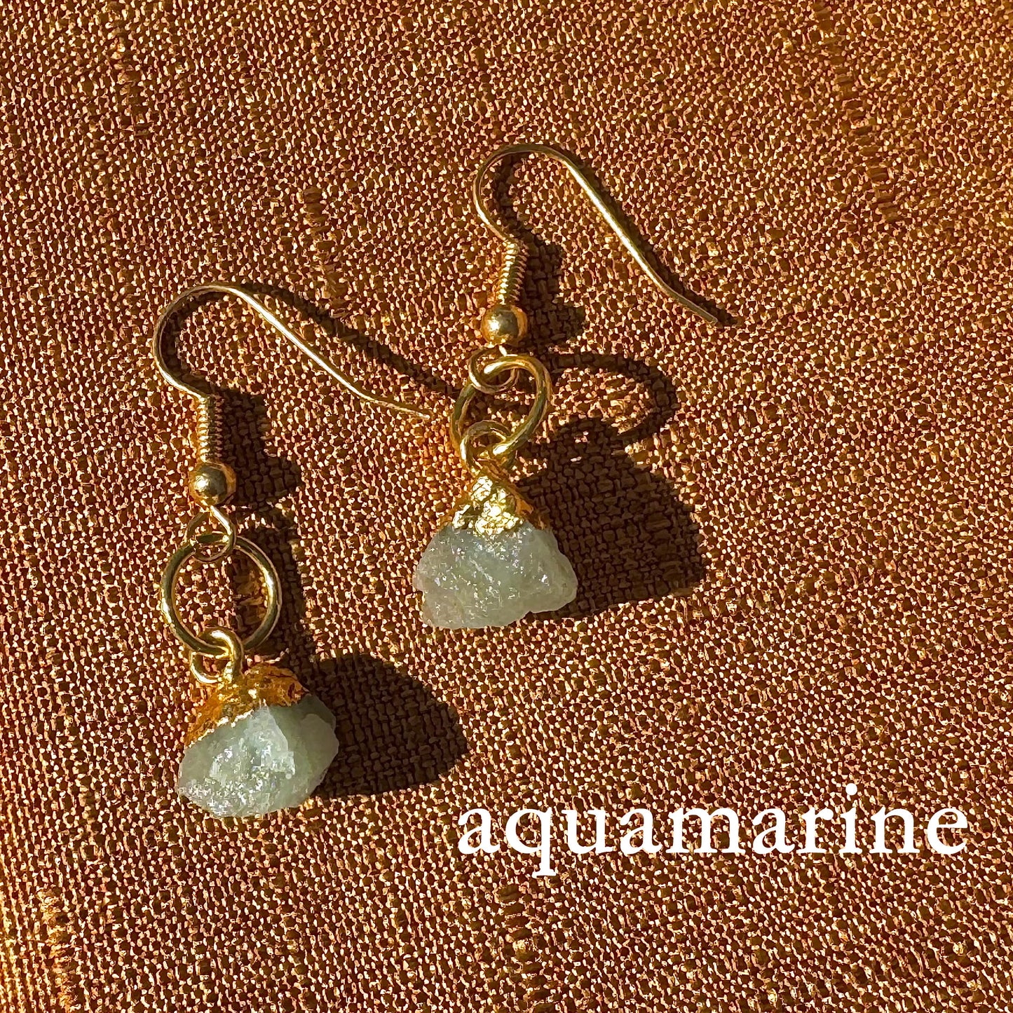 Gold earrings with aquamarine stones on a brown textured background