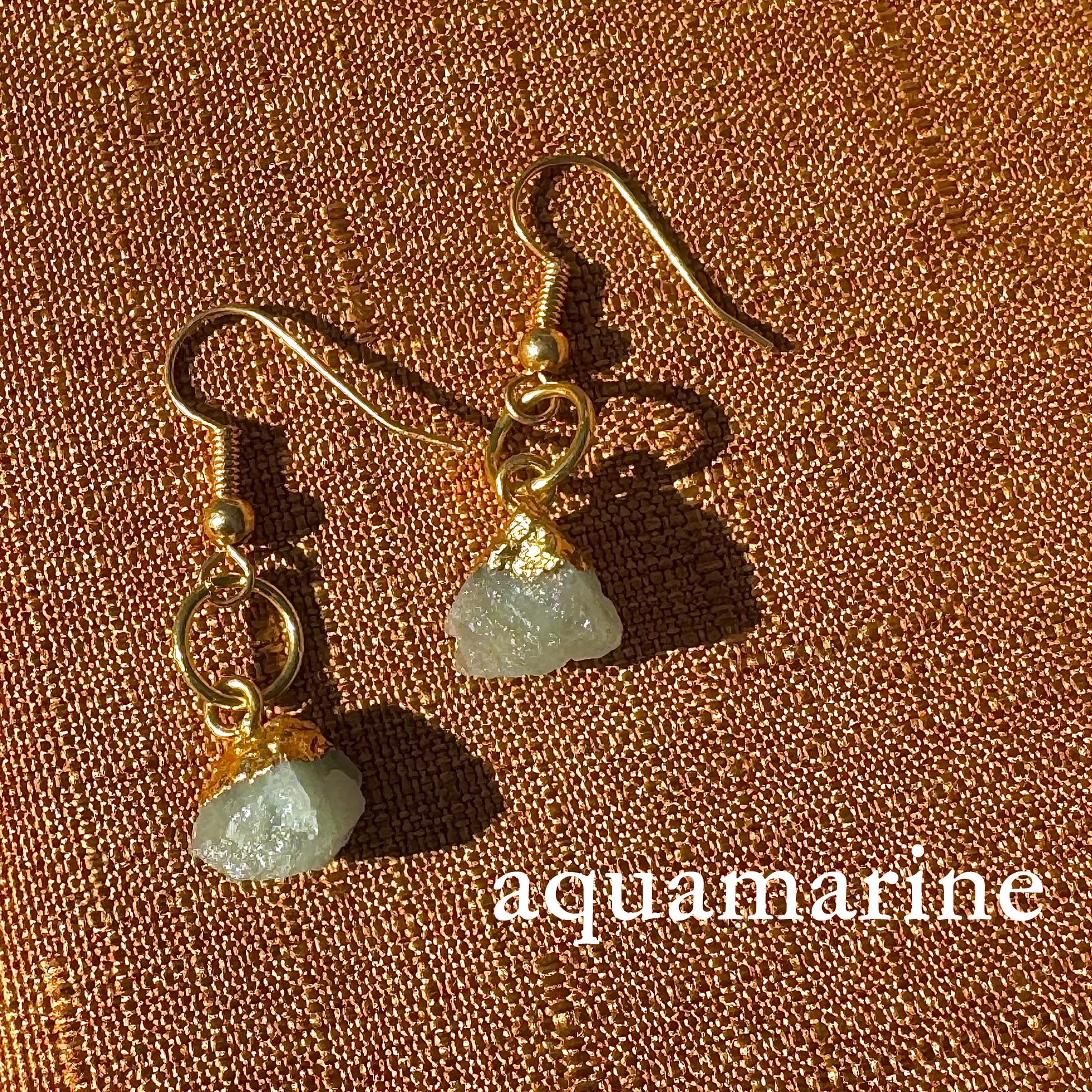 Gold earrings with aquamarine stones on a brown textured background
