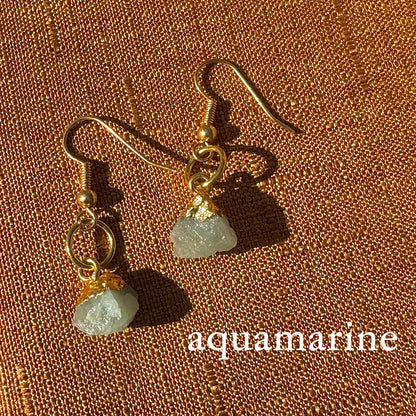 Gold earrings with aquamarine stones on a brown textured background
