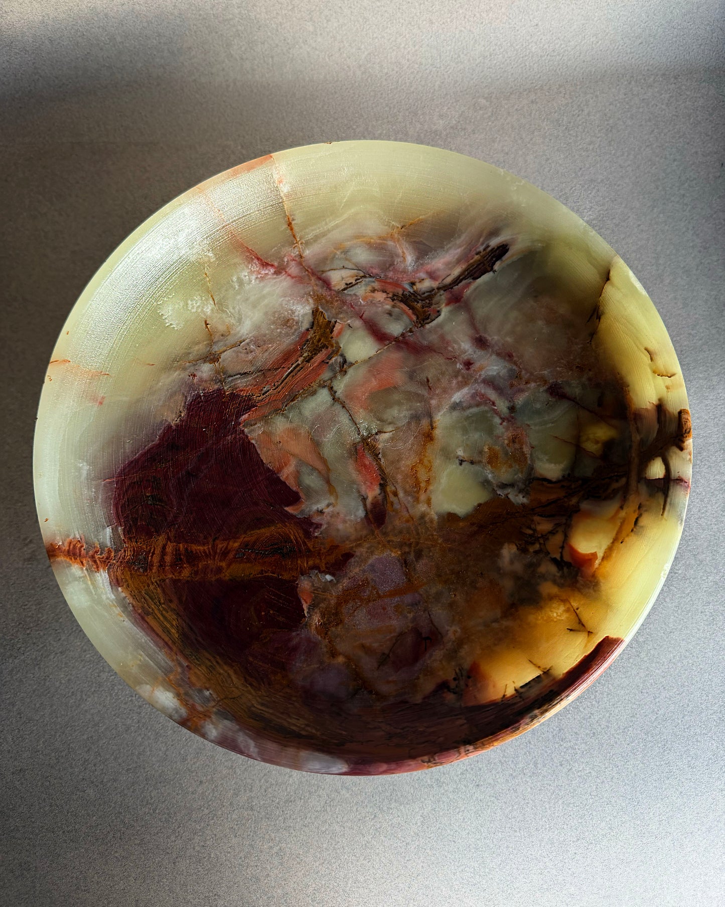 Close up detail of natural onyx bowl interior showing olive green stone with amber and plum marbling
