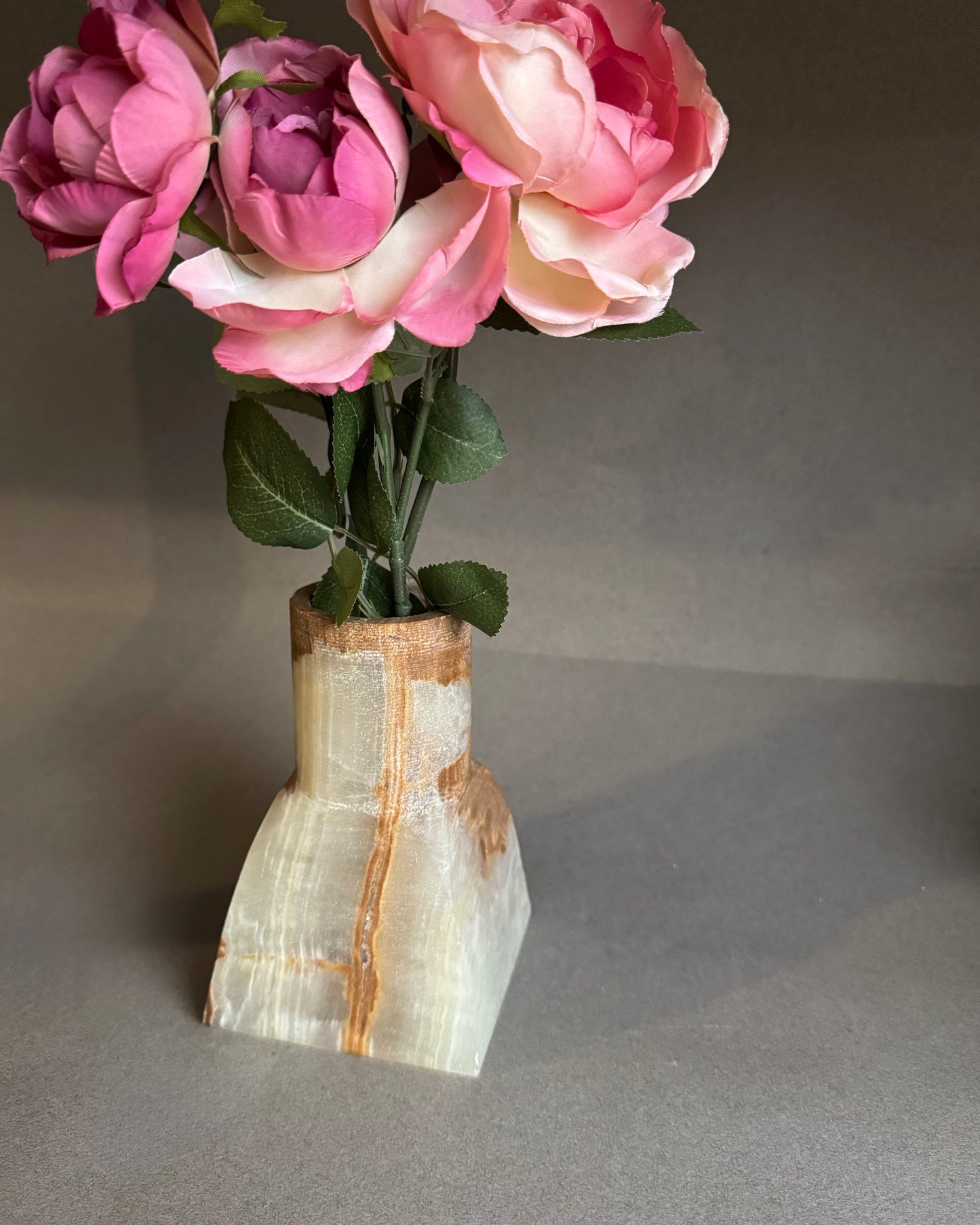 Onyx stone vase with pink flowers on a gray background