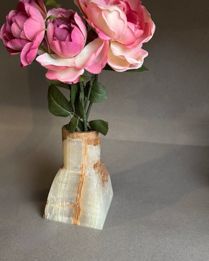 Onyx stone vase with pink flowers on a gray background