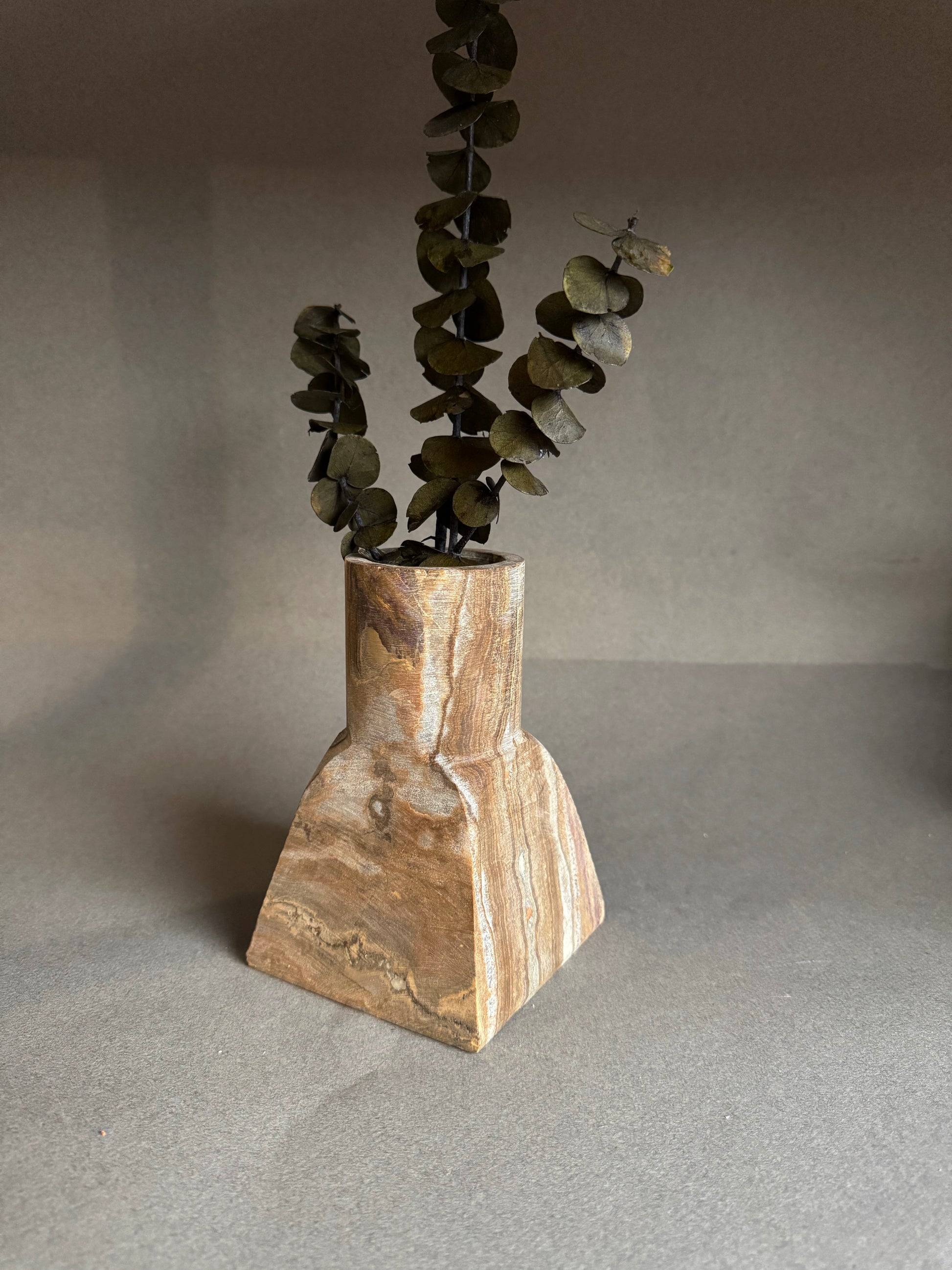 Onyx stone vase with a geometric design containing dried eucalyptus on a gray background