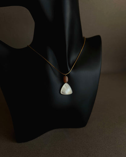 Necklace with a pendant on a black mannequin bust against a dark background Gold waterproof snake chain necklace with mother of pearl and sunstone pendant on textured background
