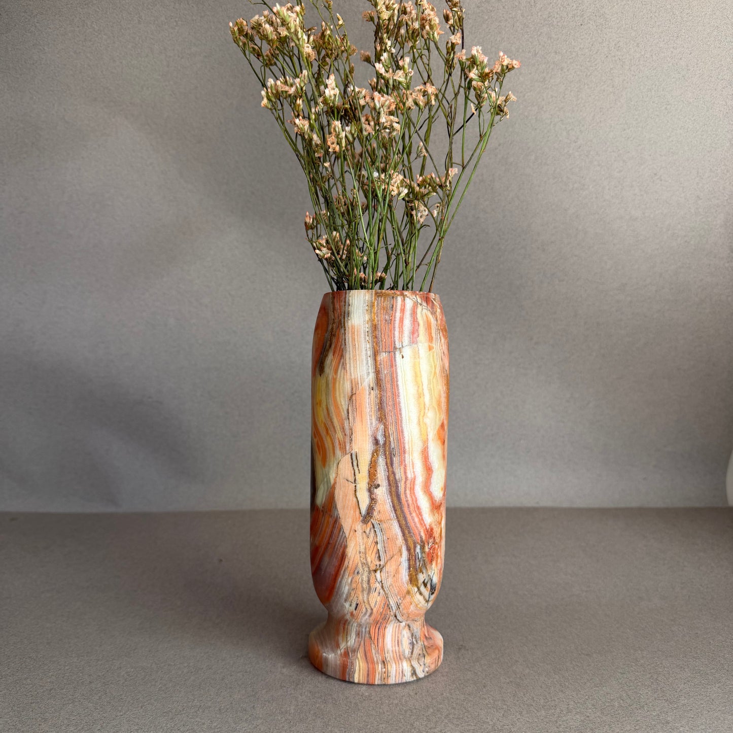 Decorative vase with a multicolored pattern containing dried flowers on a gray background