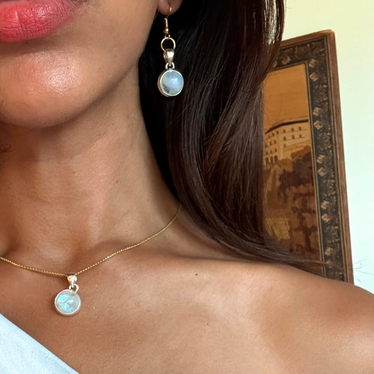 Close-up of a person wearing gold MOONSTONE earrings and moonstone necklace with a blurred background