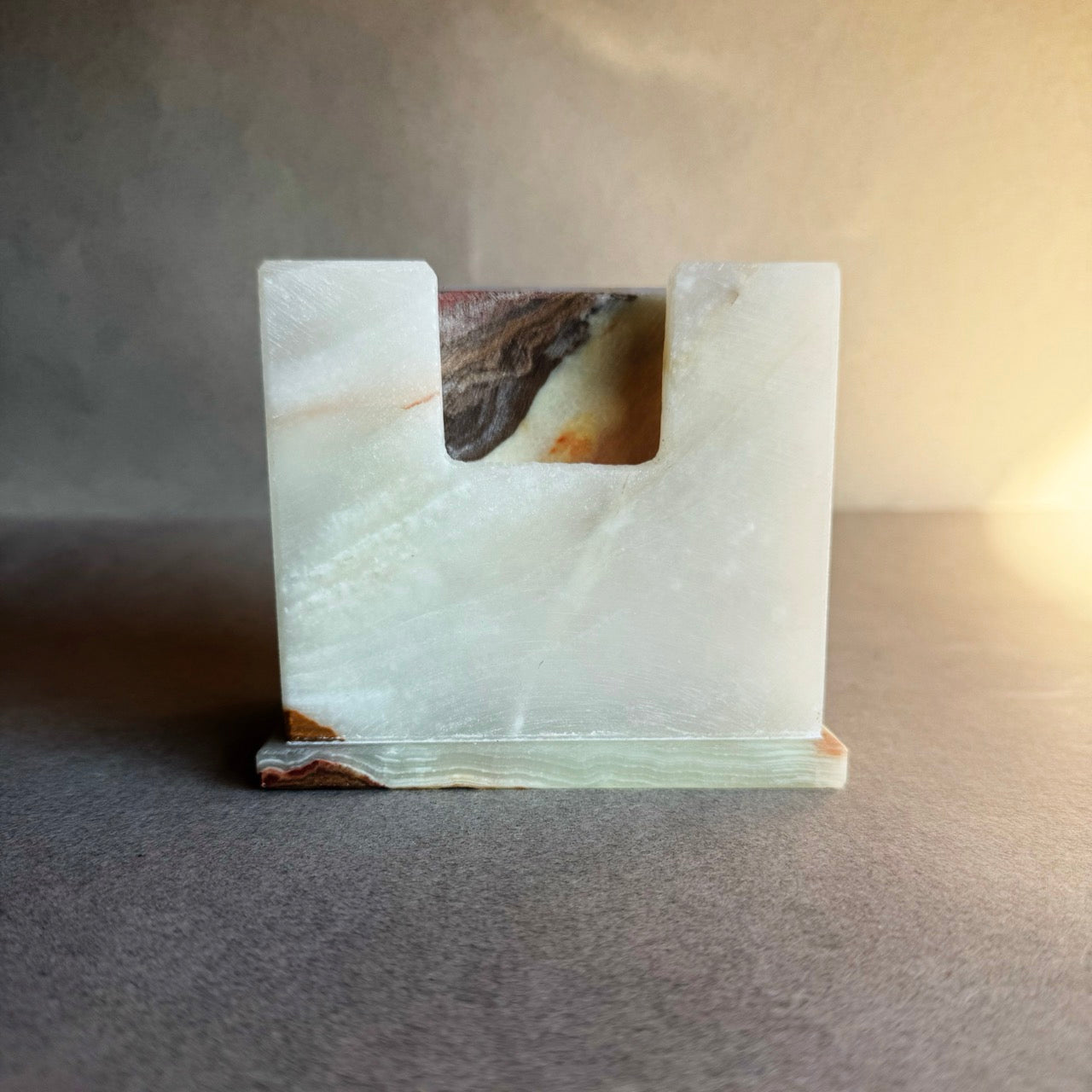 Hand-carved stone coaster holder in ivory and cream with natural brown and rust patterns, shown from angle.