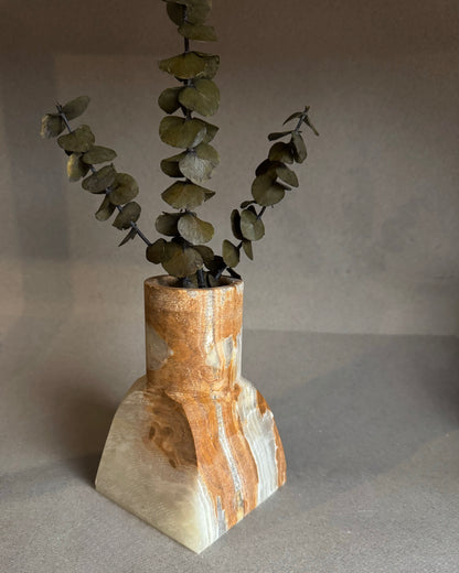 Decorative vase with a natural stone design holding a branch of eucalyptus against a plain background