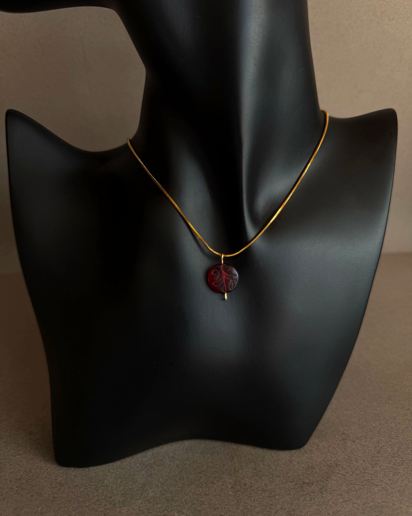 Necklace with a red pendant on a black mannequin bust against a neutral background Close-up of engraved red garnet bead pendant with translucent crimson tones
