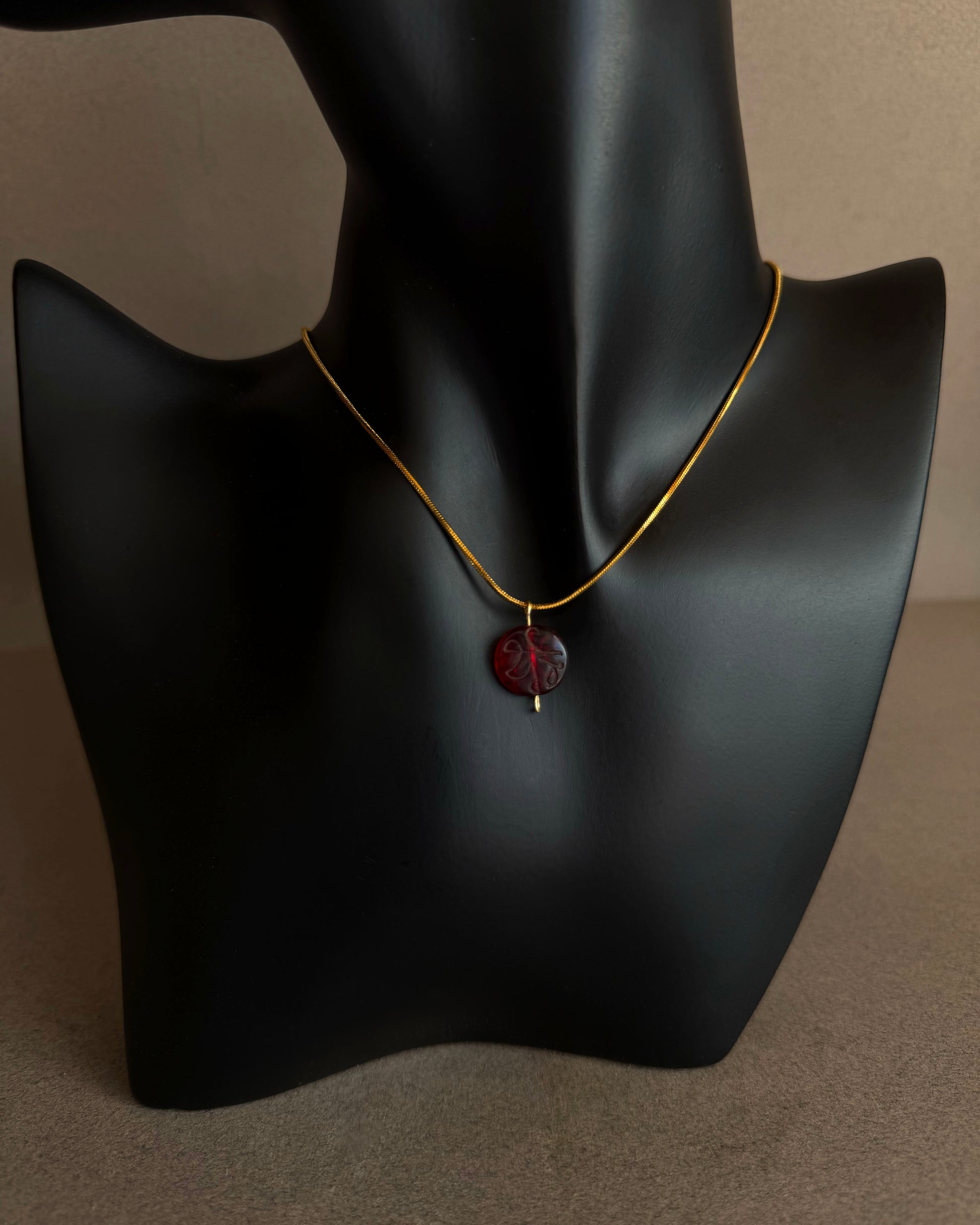 Necklace with a red pendant on a black mannequin bust against a neutral background Close-up of engraved red garnet bead pendant with translucent crimson tones
