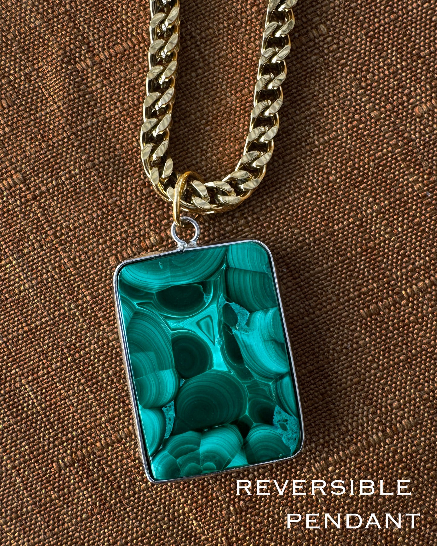 Reversible pendant with green marbled design on a gold chain against a brown textured background.