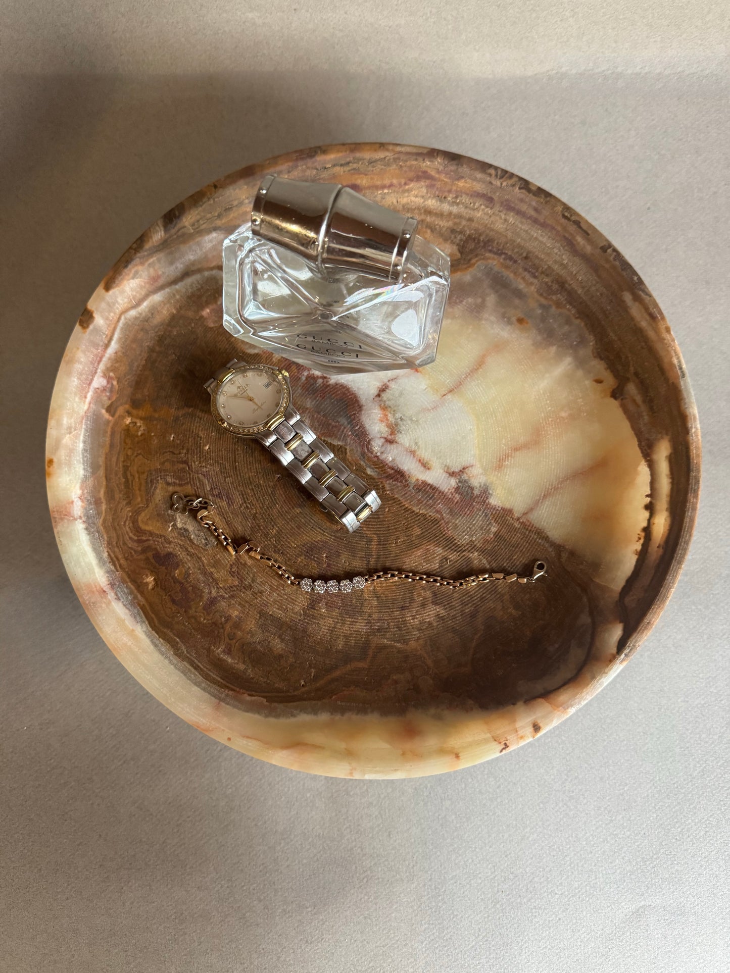 Jewelry including a bracelet, necklace, and small bottle on a decorative stone surface.