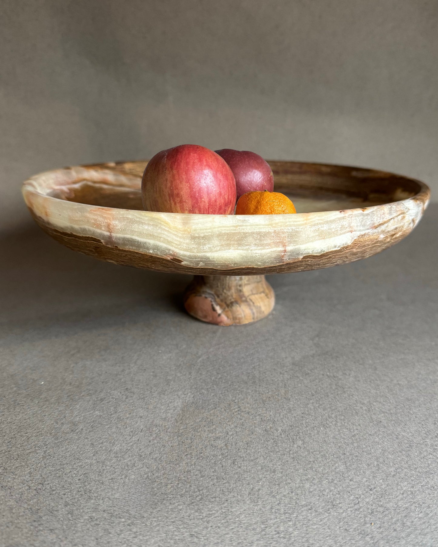 Onyx stone pedestal bowl with fruits on a gray background