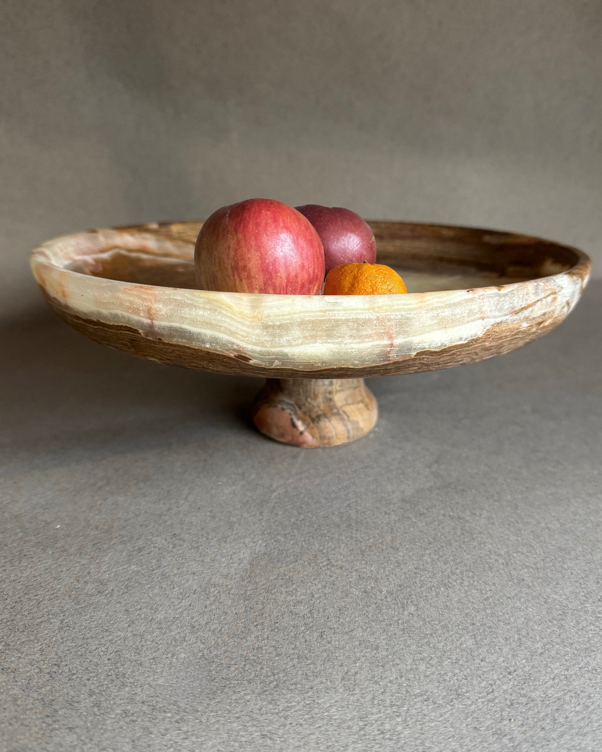 Onyx stone pedestal bowl with fruits on a gray background