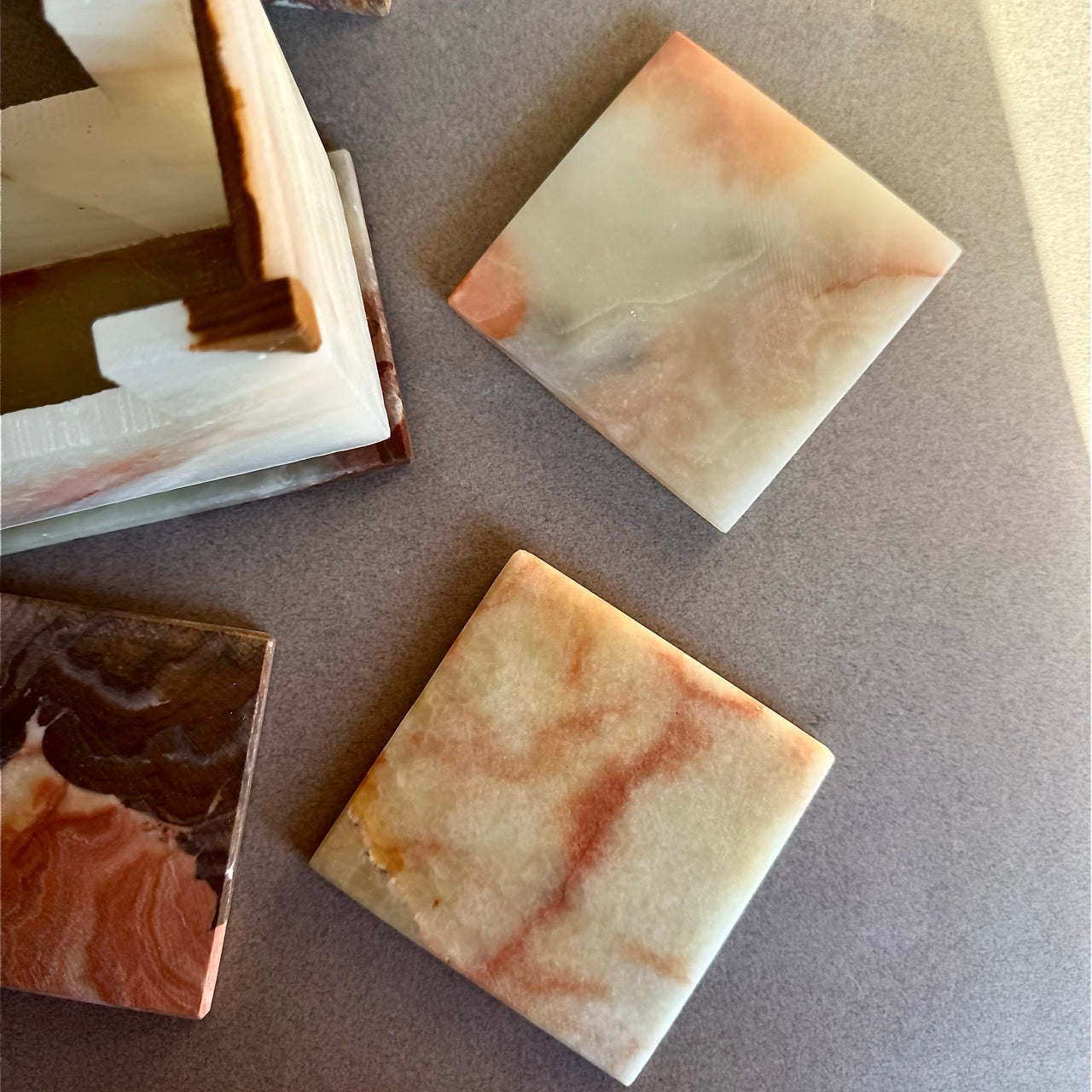 Onyx coaster set with six square stone coasters and matching holder, colors in ivory, cream, honey, and rust marbling.