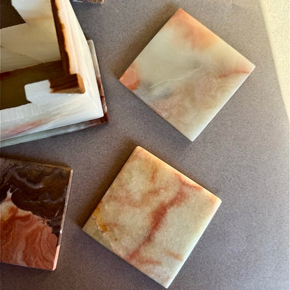 Onyx coaster set with six square stone coasters and matching holder, colors in ivory, cream, honey, and rust marbling.