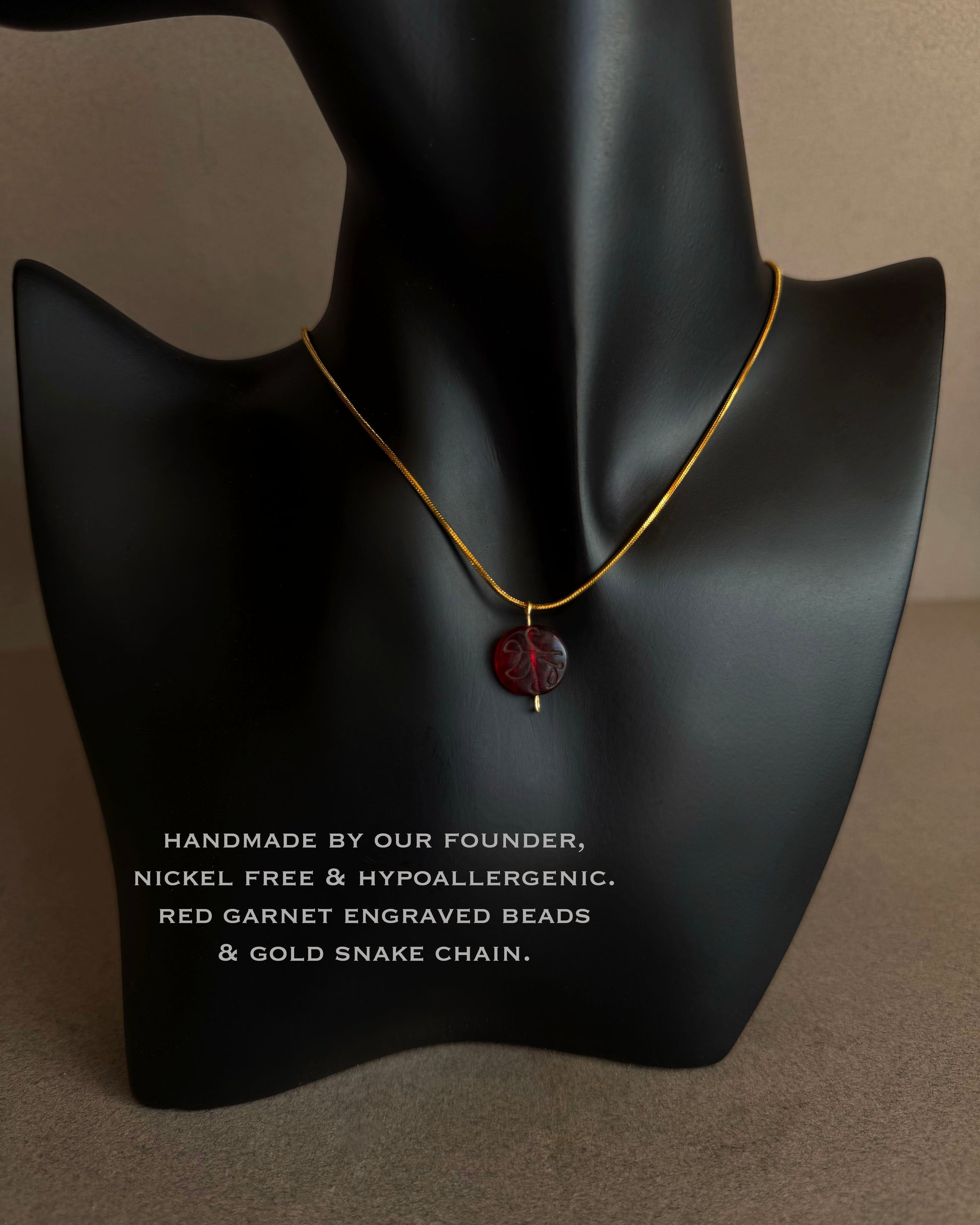 Necklace with red garnet engraved beads and gold snake chain on a black mannequin bust.