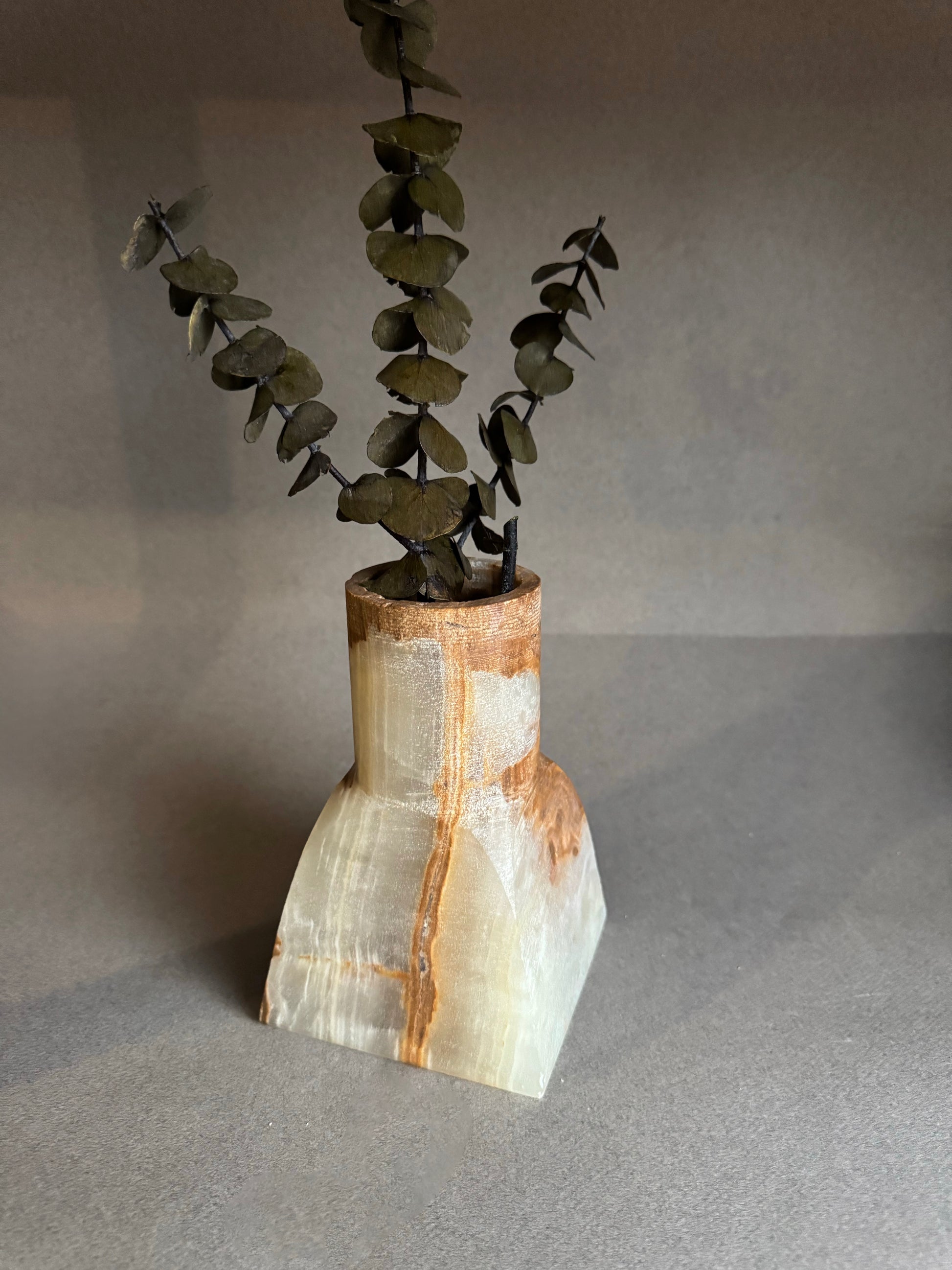 Stone vase with a natural finish holding a branch on a gray background