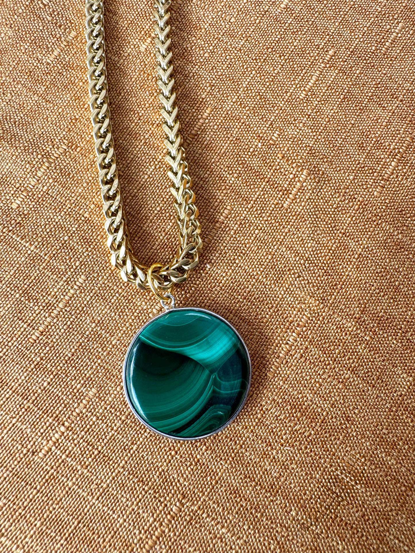 italian franco chain with a green pendant on a beige fabric background