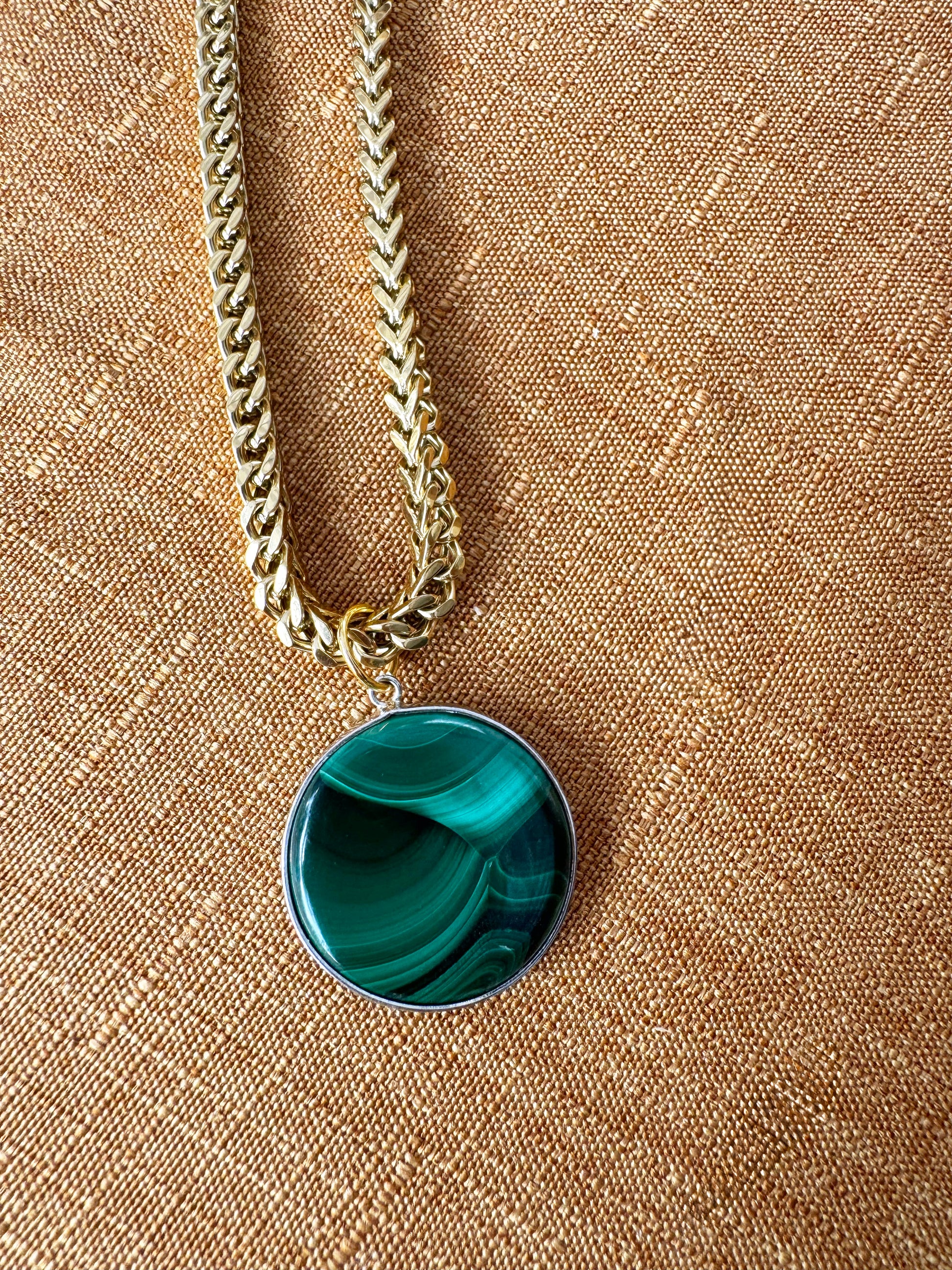 italian franco chain with a green pendant on a beige fabric background