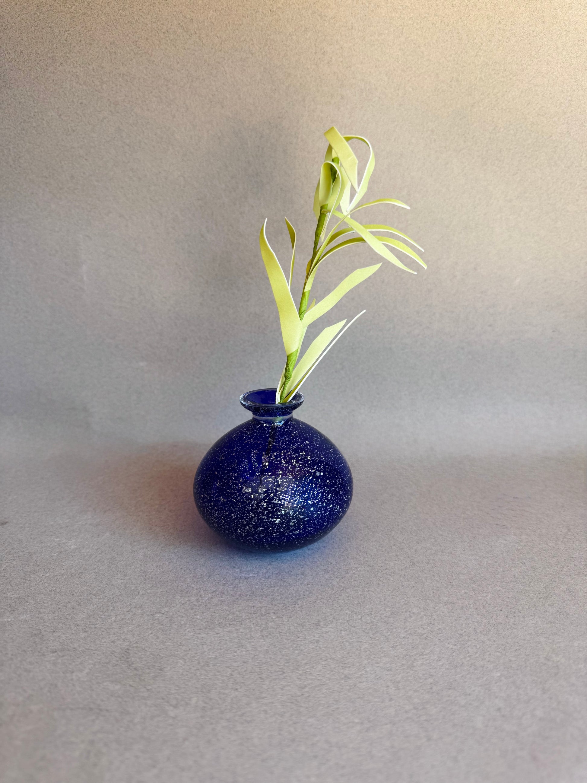 Blue speckled vase with a single green plant on a gray background