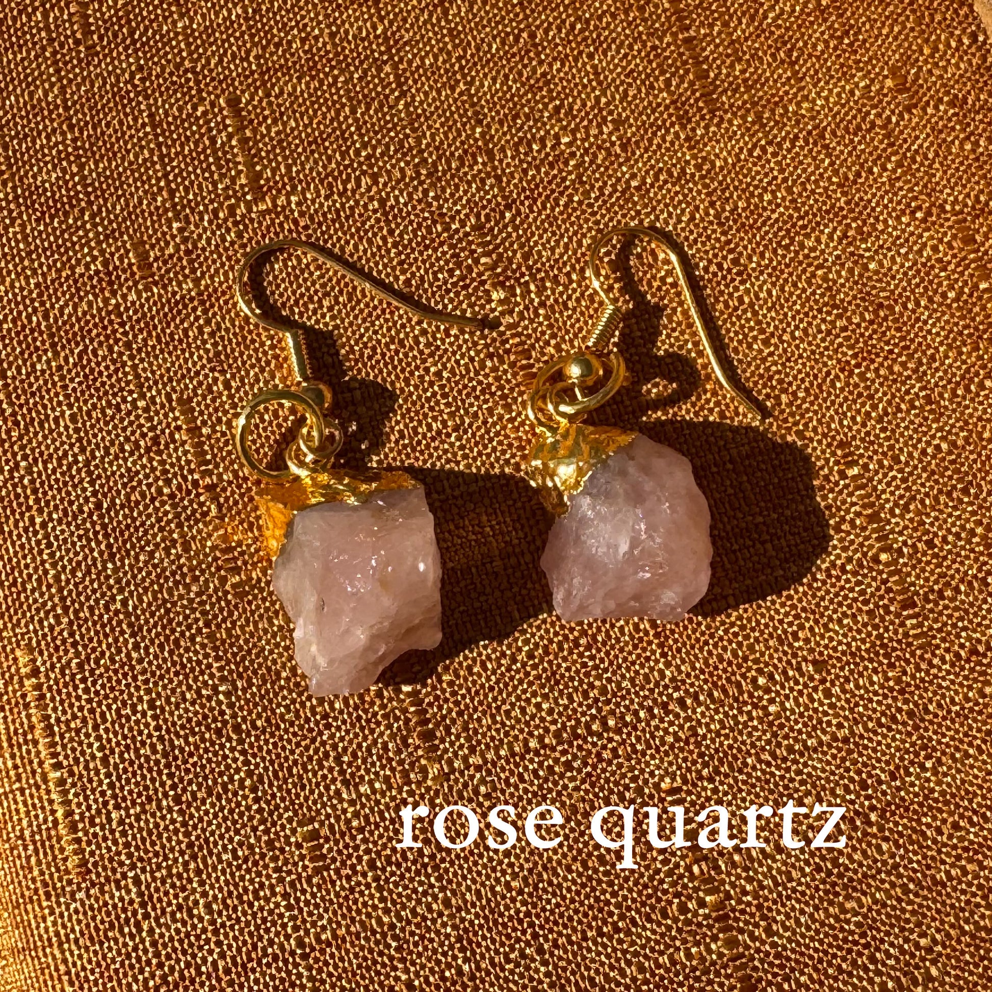 Rose quartz earrings with gold hooks on a brown fabric background