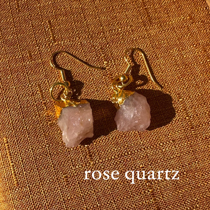 Rose quartz earrings with gold hooks on a brown fabric background