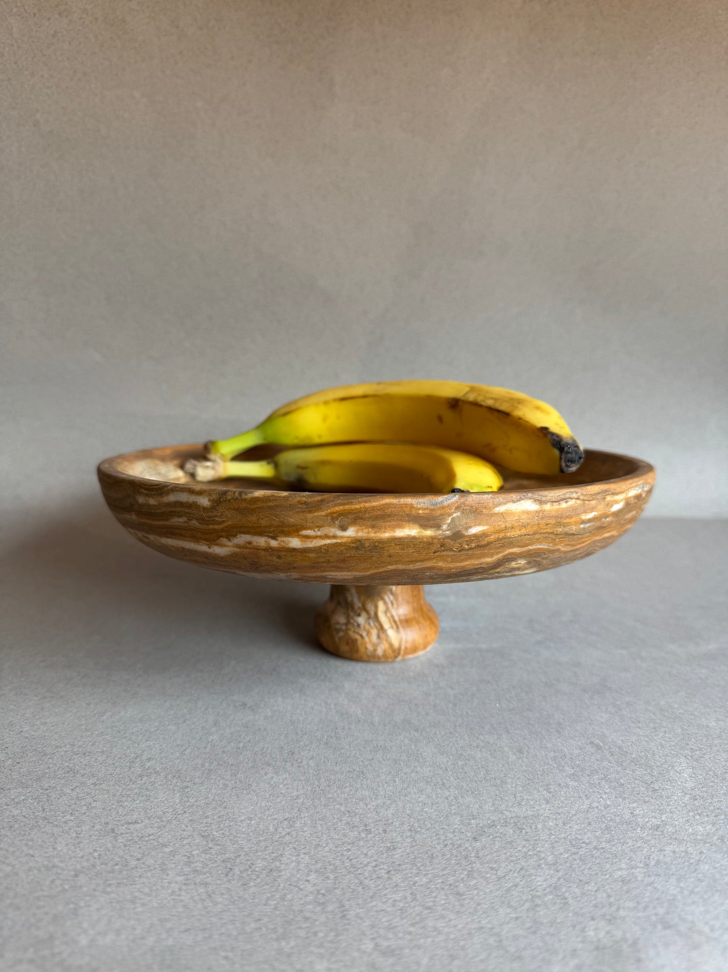 Stone bowl with a foot holding bananas on a neutral background