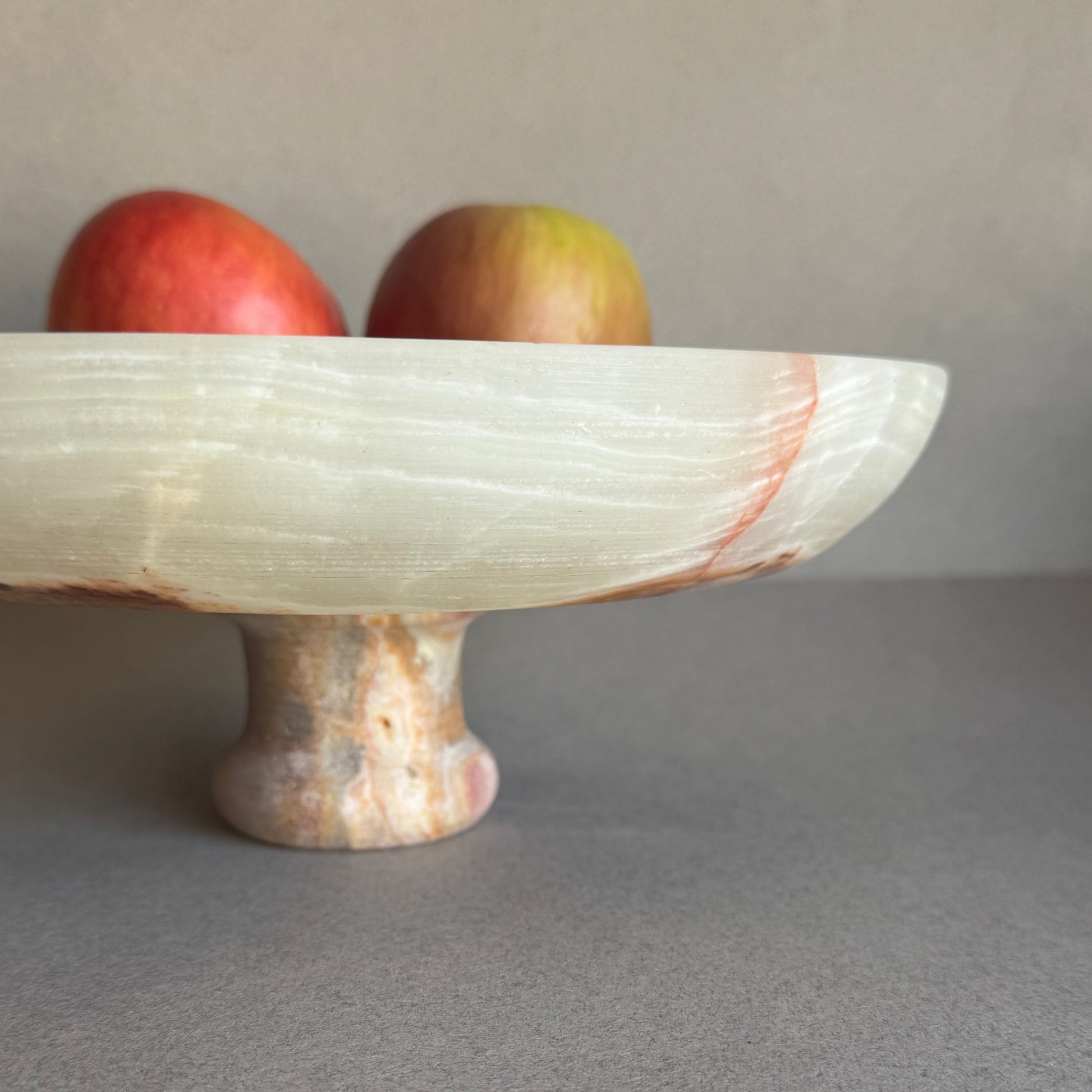 Cream and sage onyx bowl styled on a dining table with fruit, highlighting its footed base and natural translucency