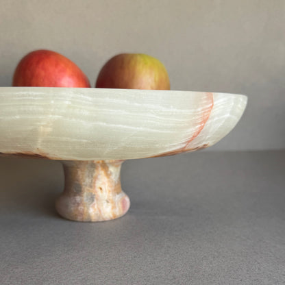 Cream and sage onyx bowl styled on a dining table with fruit, highlighting its footed base and natural translucency