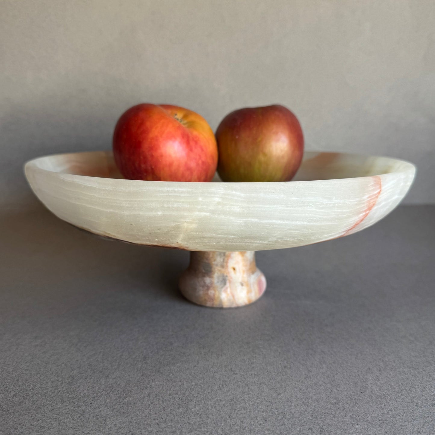Cream and sage onyx bowl styled on a dining table with fruit, highlighting its footed base and natural translucency