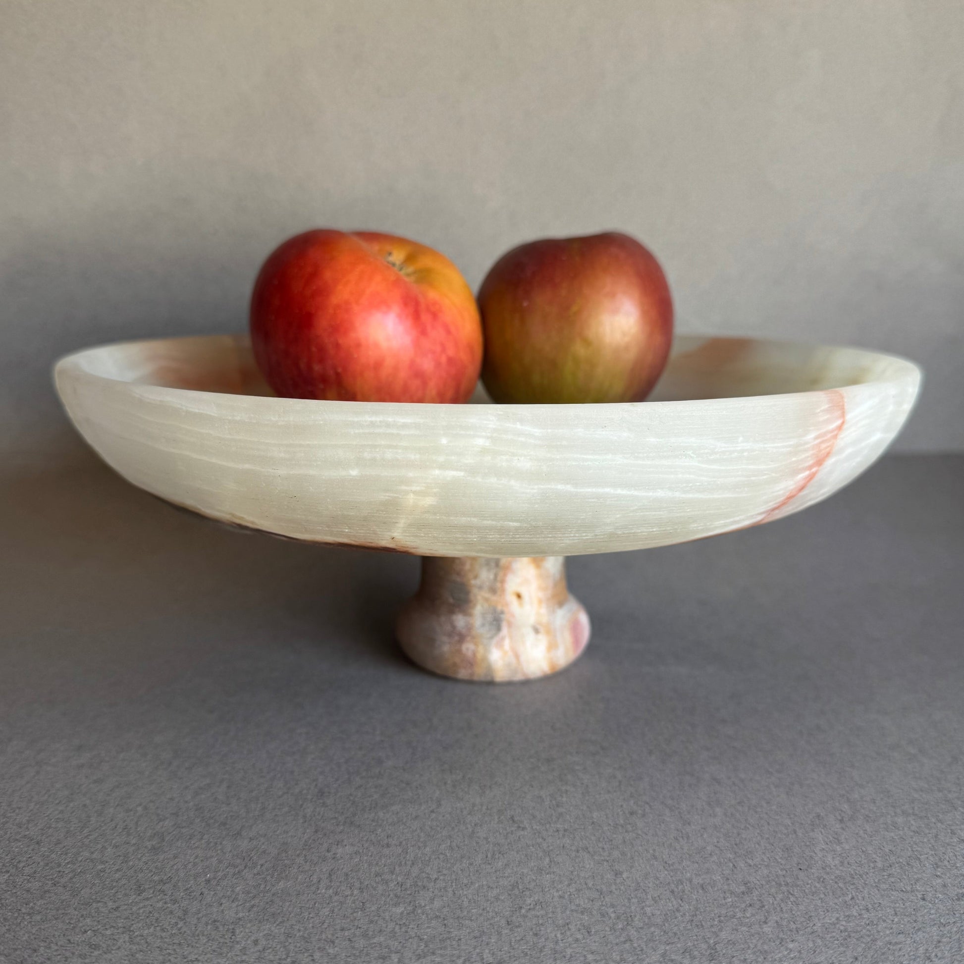 Cream and sage onyx bowl styled on a dining table with fruit, highlighting its footed base and natural translucency