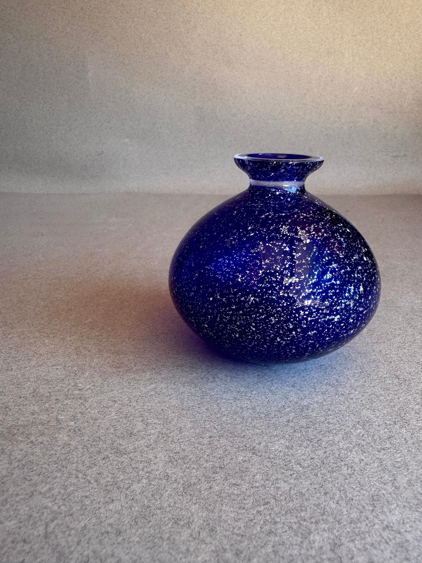 Blue speckled vase on a gray surface with a neutral background