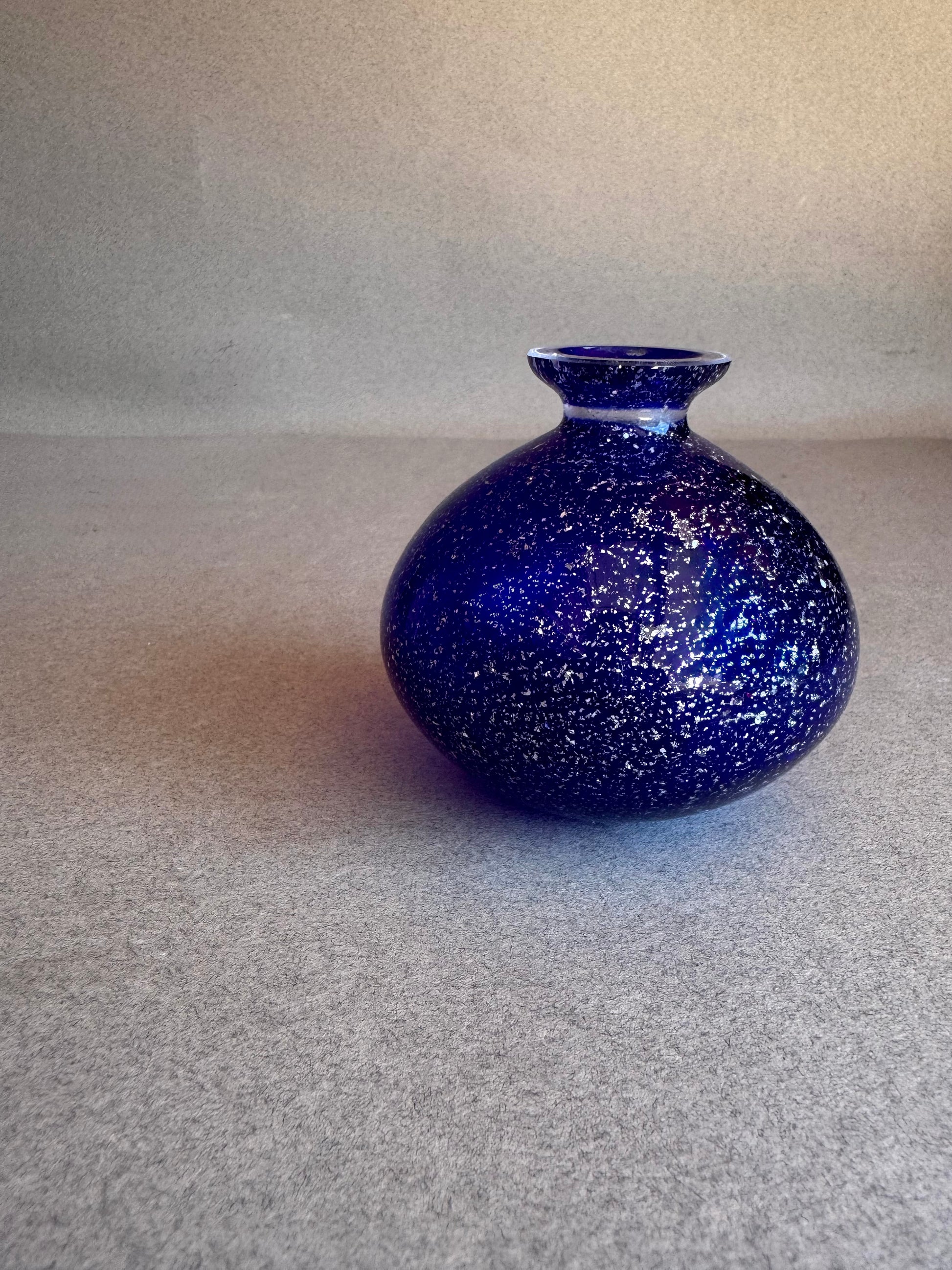 Blue speckled vase on a gray surface with a neutral background