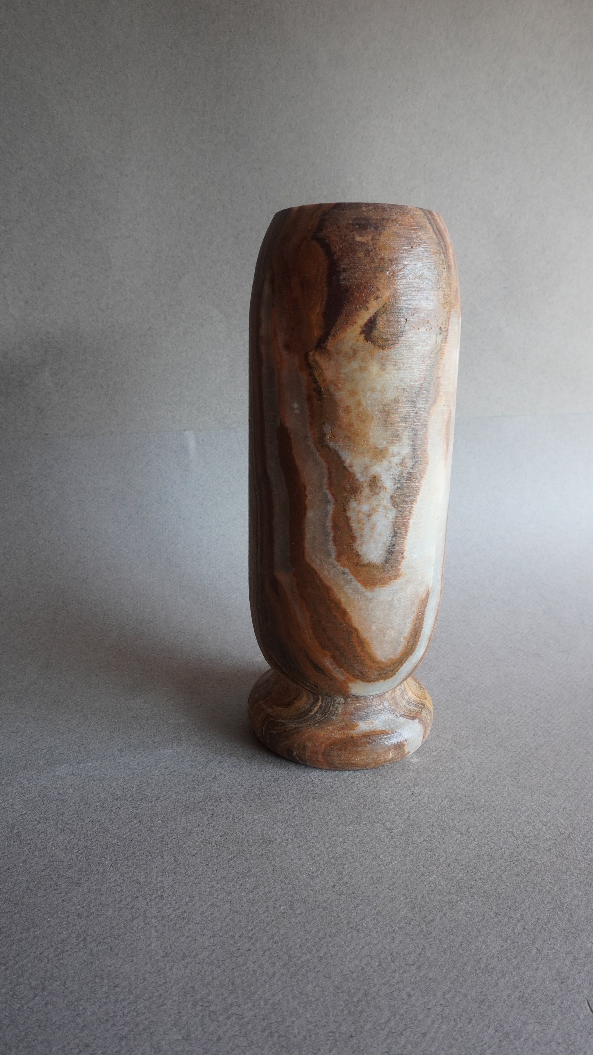 Angled view of marbled onyx vase with ivory, amber, and brown layers, one-of-a-kind stone decor piece

