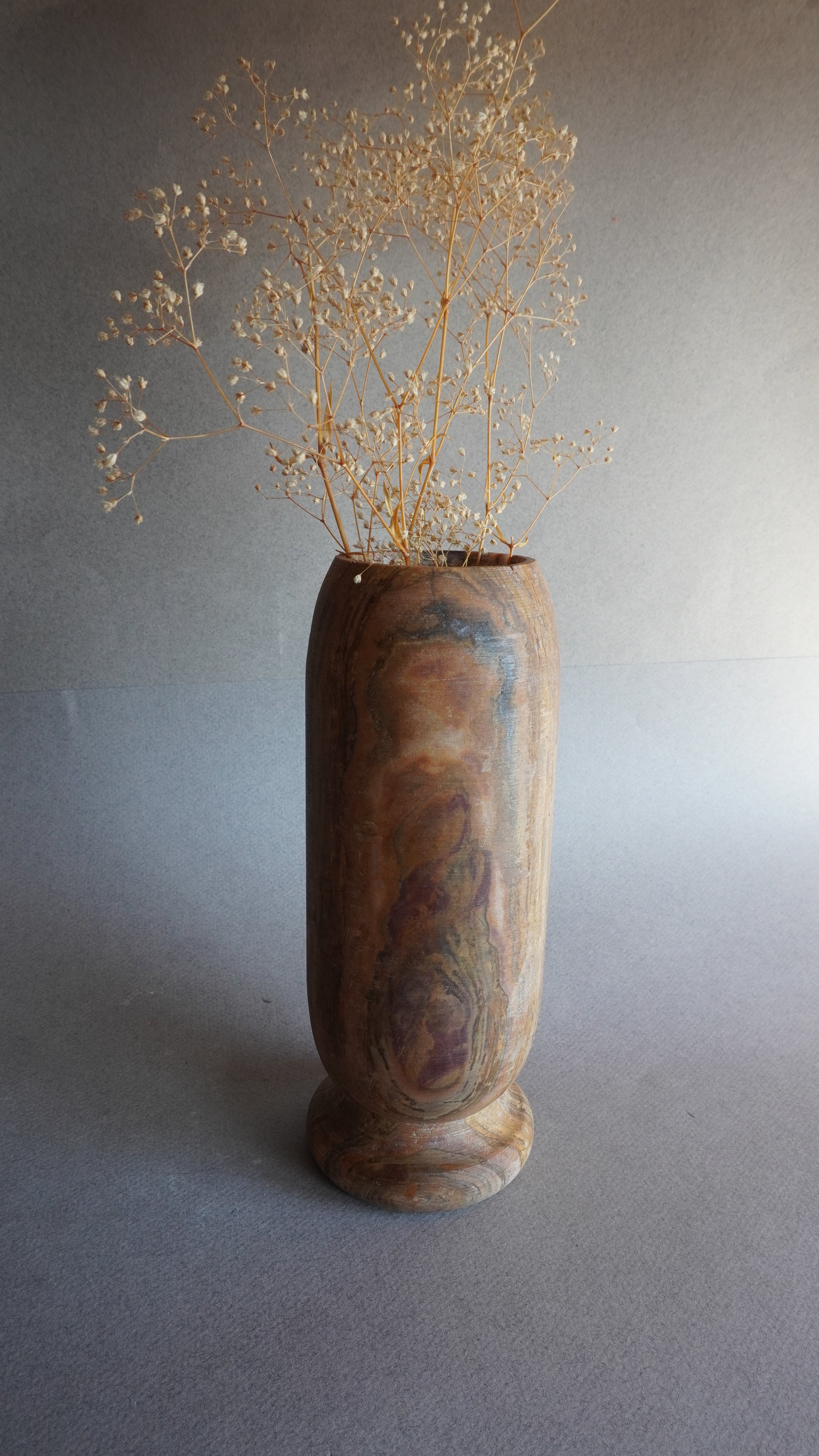 Close-up of pedestal base on tall onyx vase, showcasing unique marbled veining in brown, rust, and ivory stone
