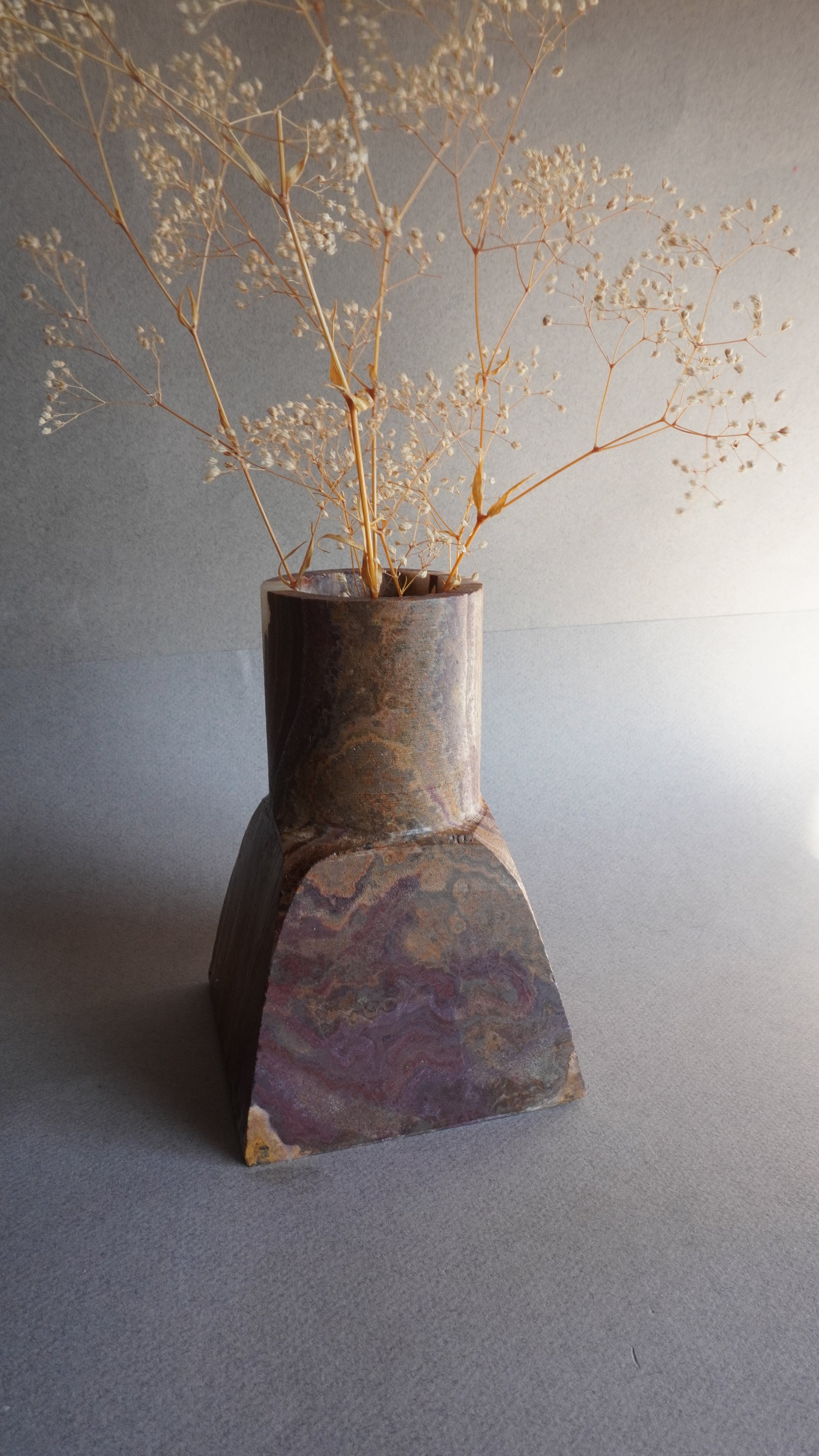 Decorative brown stone onyx vase with dried plants against a neutral background