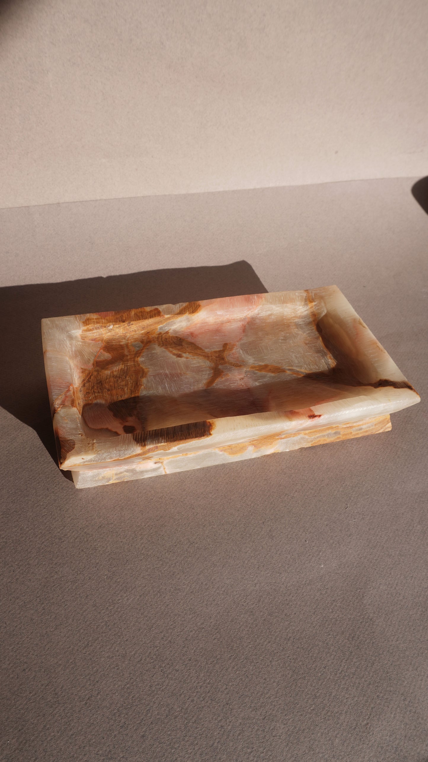 Rectangular onyx stone dish with brown and white marbled pattern on a gray surface