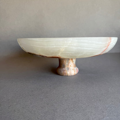 Cream and sage onyx bowl with pedestal base, partially lit to highlight stone’s translucency.