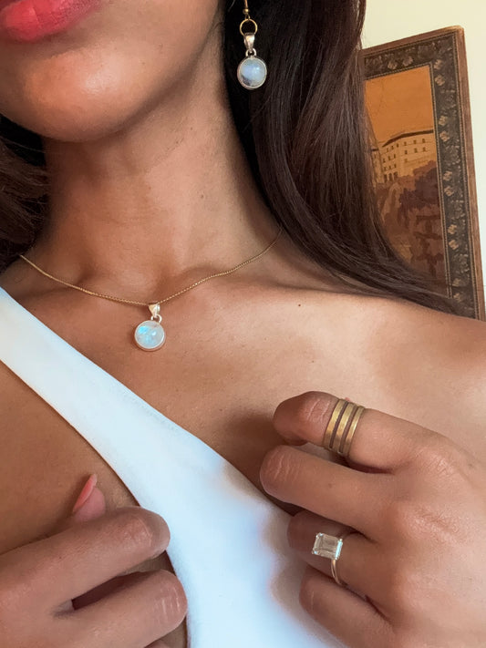 Close-up of a person wearing moonstone gold jewelry including a necklace, earrings, and ring.