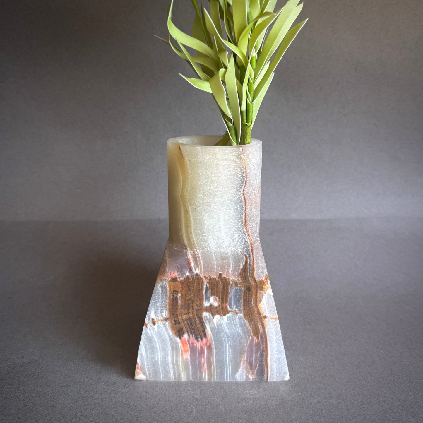 Onyx Vase with a unique design holding green plants on a gray background