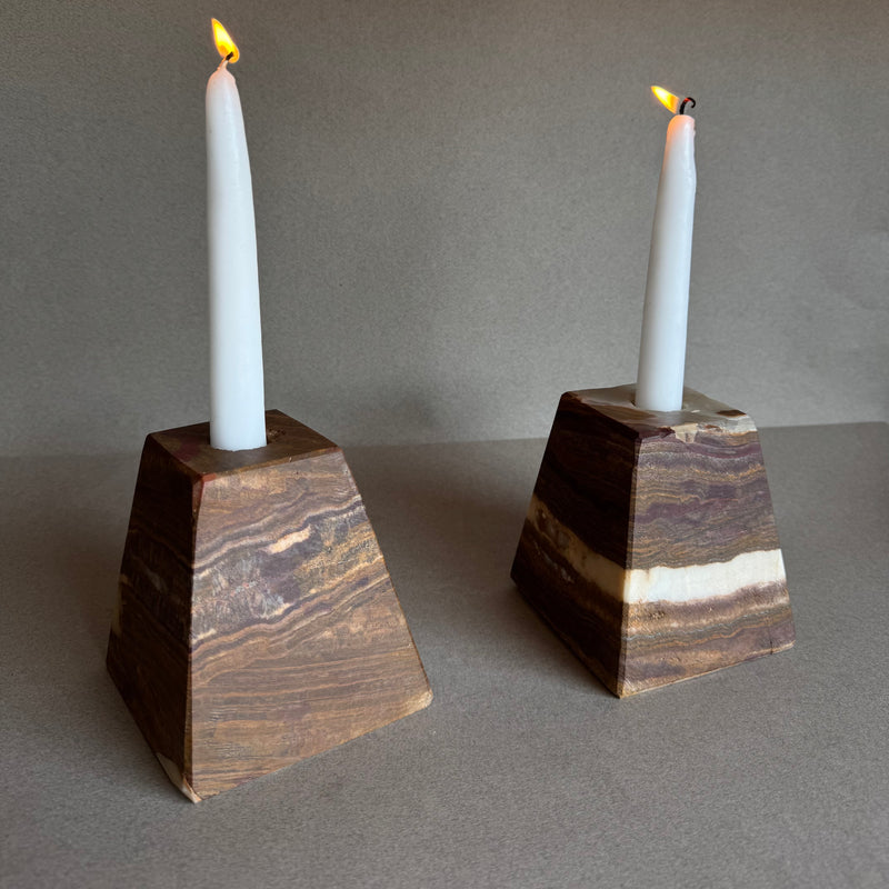 Two brown onyx pyramid candle holders with white candles on a gray background