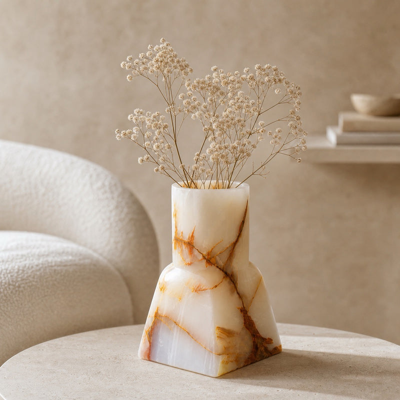 Hand-carved onyx bud vase, stepped architectural form in milk white with branching amber and gold veins, holding dried baby's breath on a round table