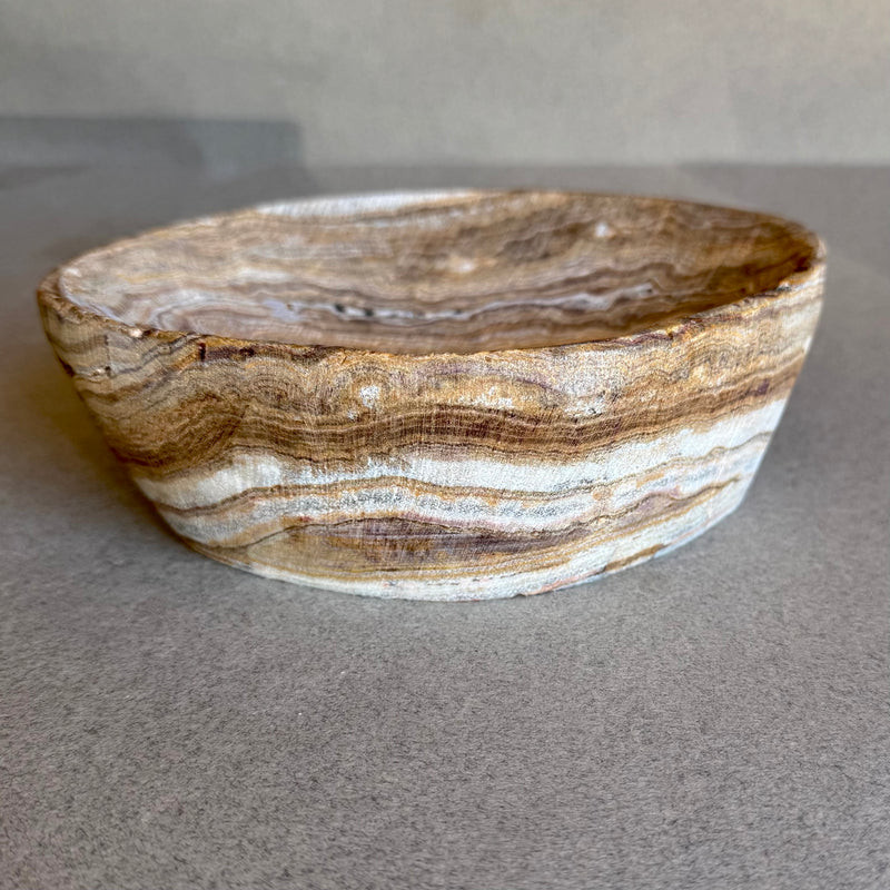 Decorative stone bowl with striped pattern on a gray surface
