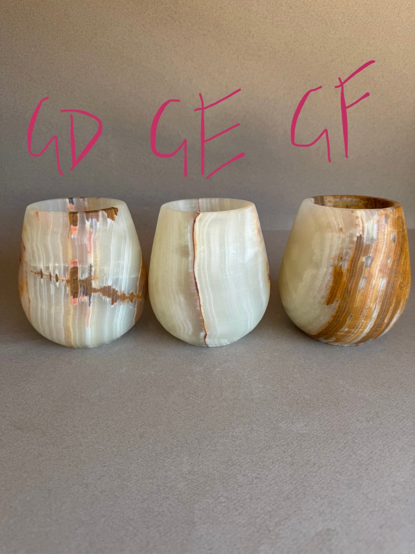 Three onyx stone cups of different shapes and sizes on a gray surface with pink text above.