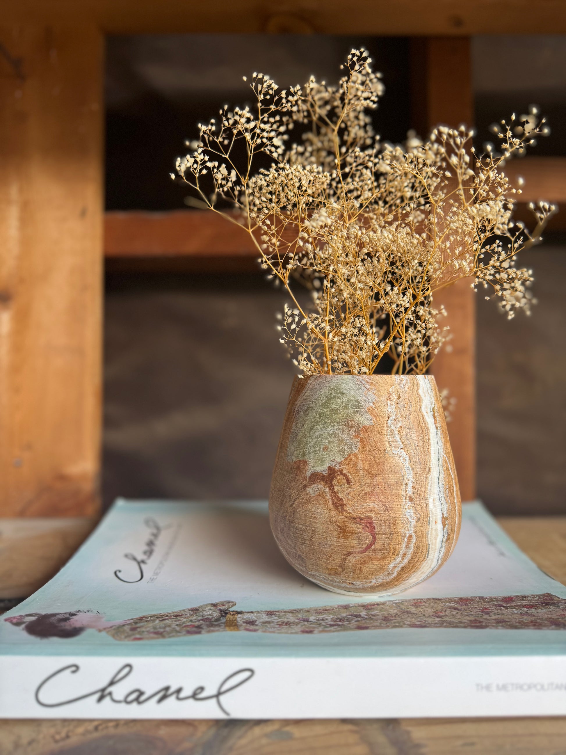 Single onyx vessel used as a vase with dried florals, placed on a Chanel coffee table book in a rustic wood setting.