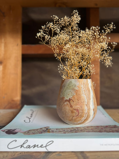 Single onyx vessel used as a vase with dried florals, placed on a Chanel coffee table book in a rustic wood setting.