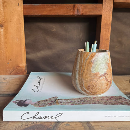 Rounded onyx vessel with soft green and rust veining holding pens, styled on top of a Chanel fashion book.