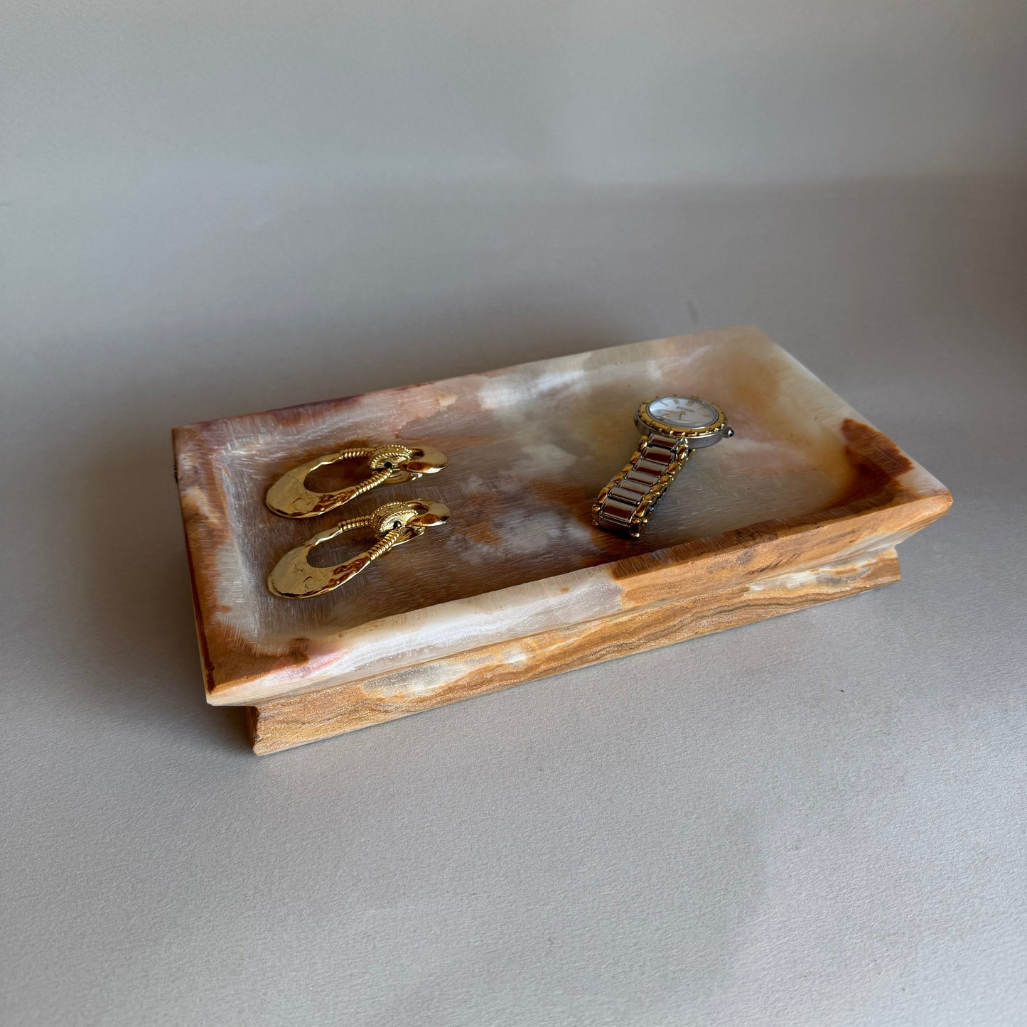Rectangular stone jewelry dish with gold earrings on a light gray background